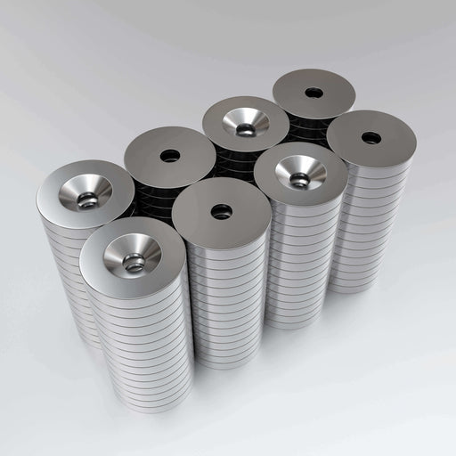 A collection of nickel-plated countersunk neodymium magnets with a hole in the center, arranged in stacks.