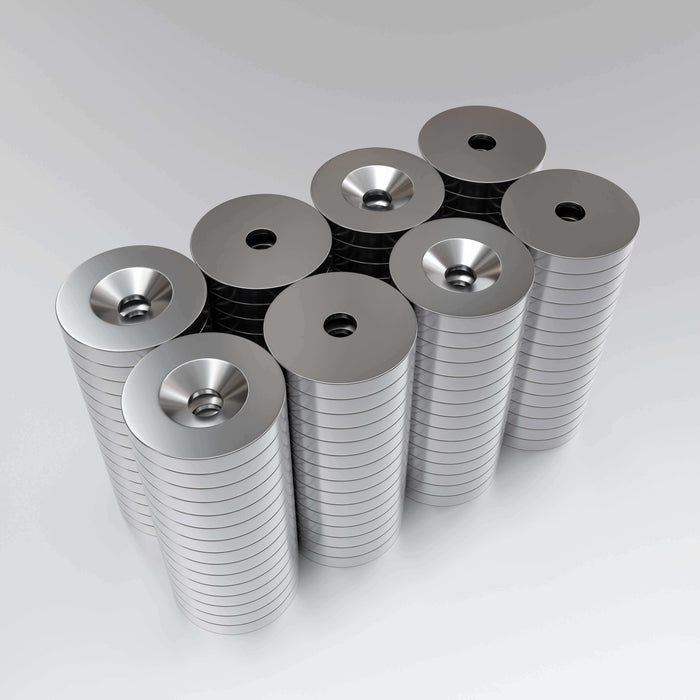 A collection of nickel-plated countersunk neodymium magnets with a hole in the center, arranged in stacks.